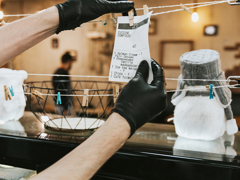 Restaurant staff hanging kitchen order ticket with gloves using string line system, supported by reliable restaurant POS support