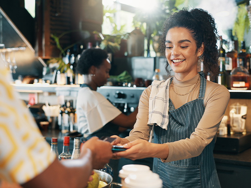 Smiling restaurant staff using mobile POS payment system behind the bar with support from the restaurant POS help desk.